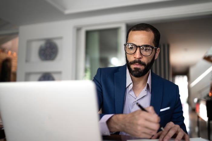 Serious person looking at laptop and writing note.
