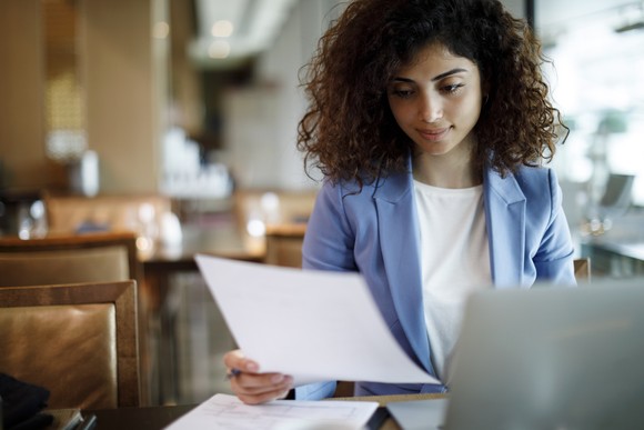 Person reviewing a document while working at a laptop.