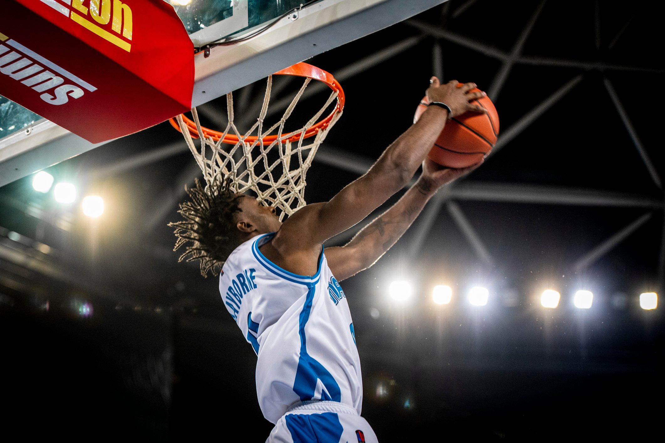 A player does a reverse dunk into a basketball hoop. 