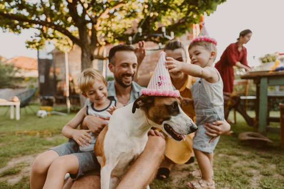 Dad with two kids and dog wearing party hat. 