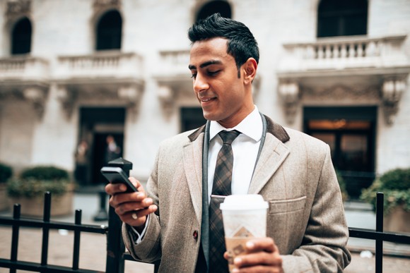 Person looking at phone in business suit holding a coffee in the street.