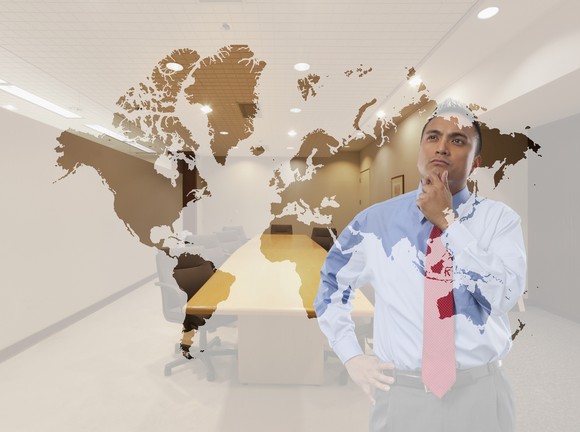 A businessman looks at a map of the world as he touches his chin thoughtfully.