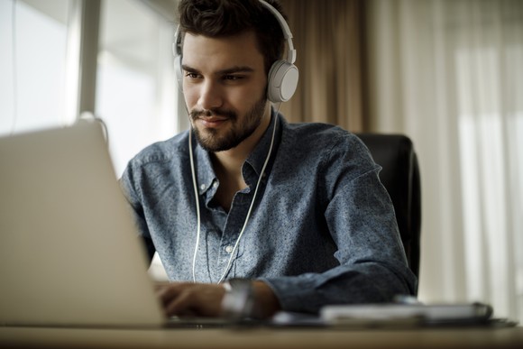 Person researches stock information on their laptop while wearing headphones.