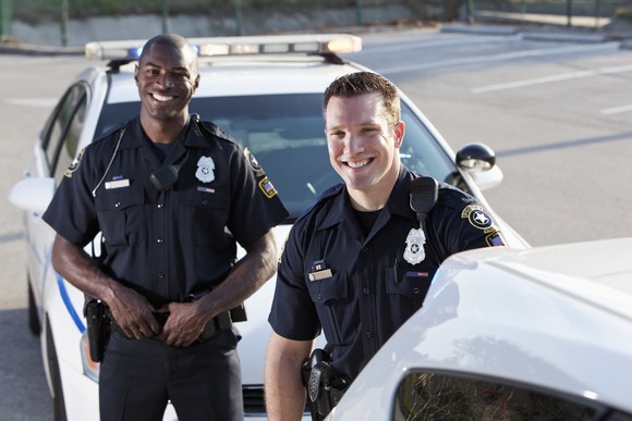 Two police officers standing by their cars and smiling.
