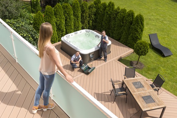 A person looking over a balcony at decking made of recycled material and two repairmen fixing a hot tub.
