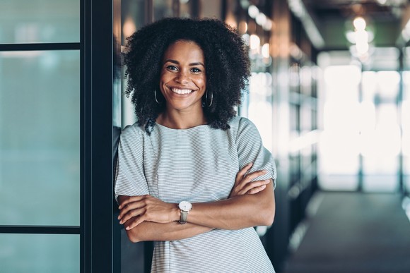 A smiling person leaning up against a wall. 