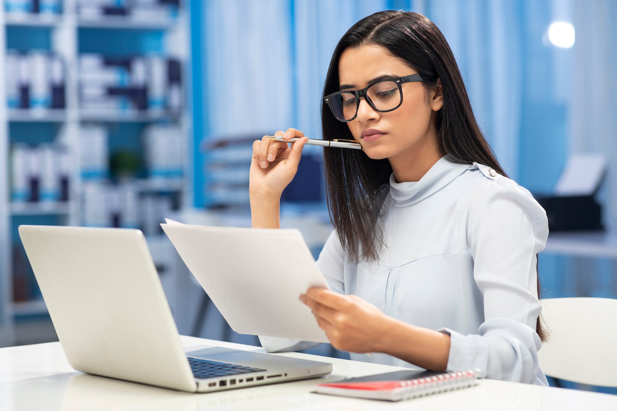 A young person perusing some papers and a laptop computer.
