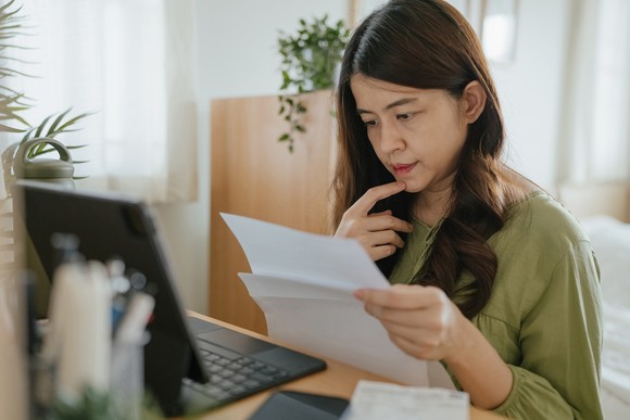 Person looking at papers in front of computer and touching chin.