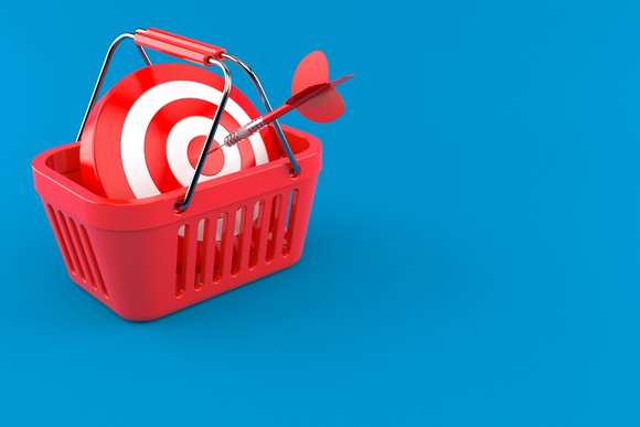 A red shopping basket holding a round target with a dart in the bull's eye.
