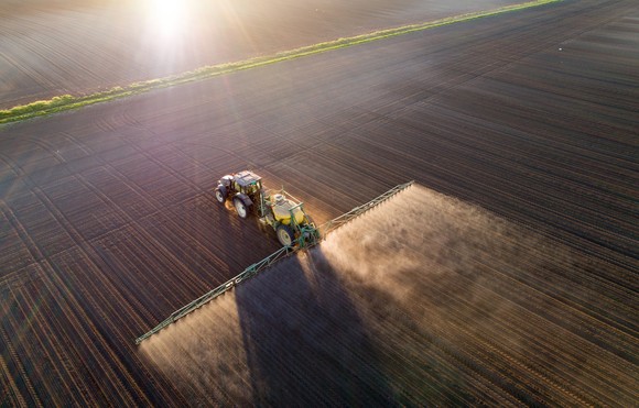 Tractor dusts crops with fertilizer in open field.