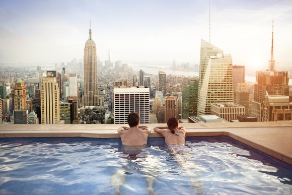 Two people in a pool overlooking a city.