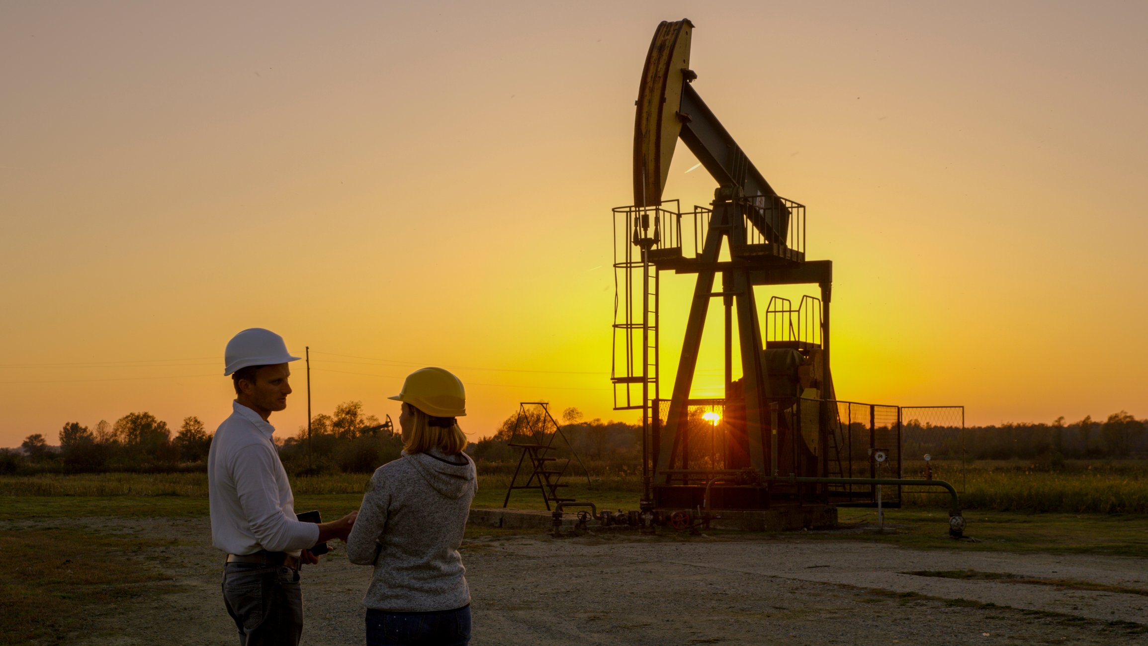Two workers have a discussion near a pumpjack.