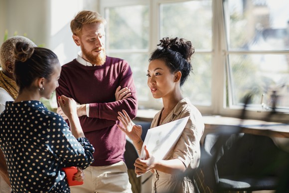 Office workers stand together and strategize at an office meeting.