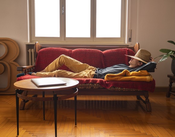 A person with a hat over their eyes, lying on a couch.