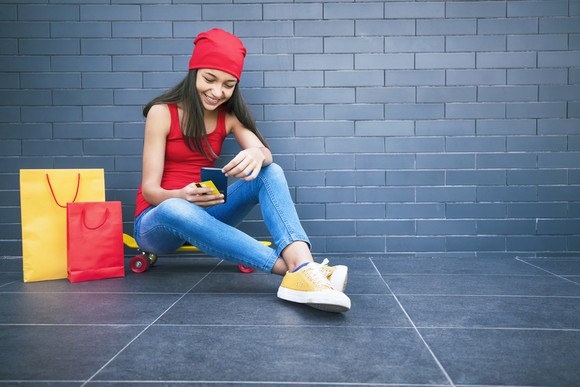 Shopper holding cellphone while sitting next to shopping bags.