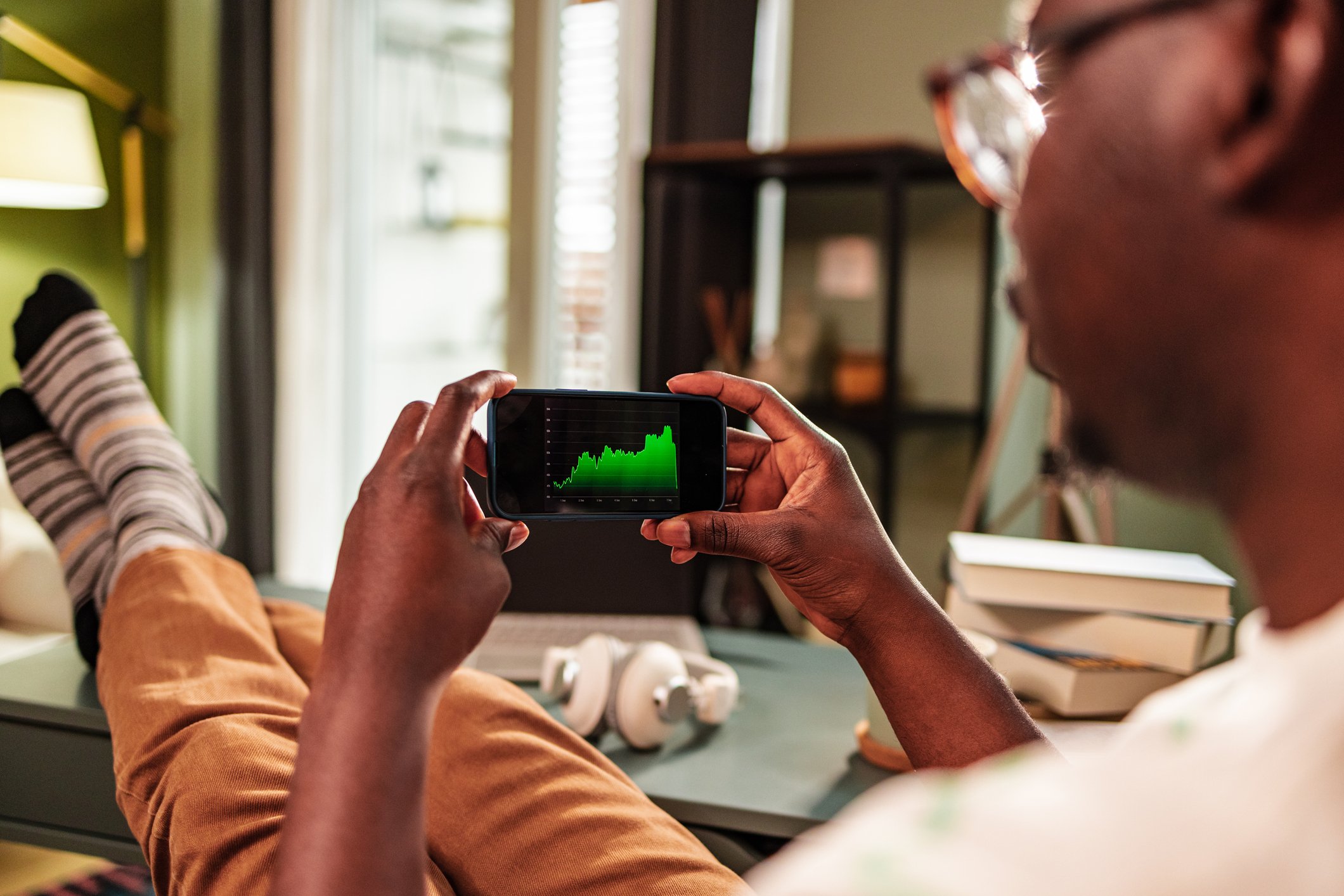 A person at home using a smartphone to look at a green stock chart.