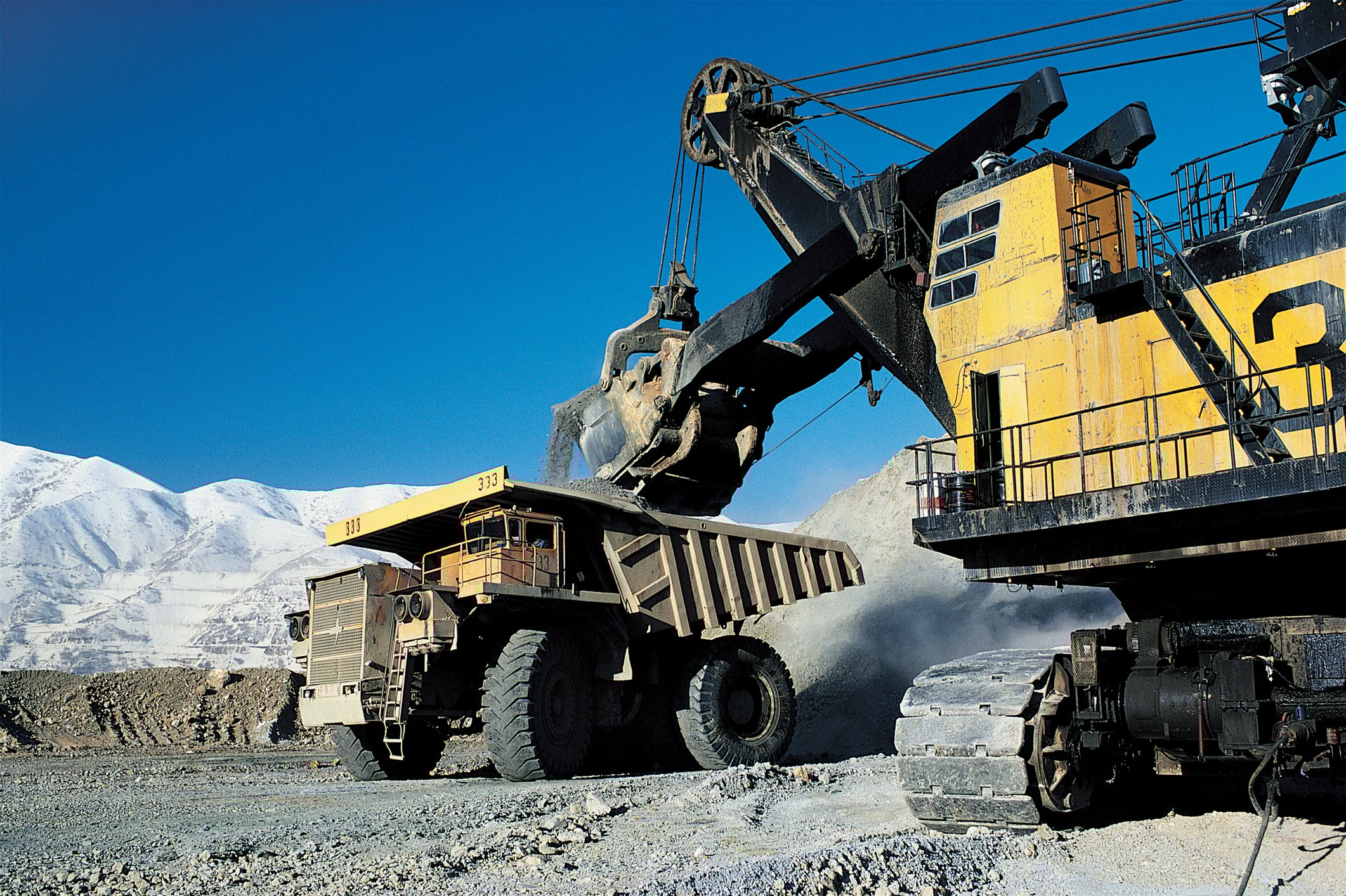 A mining excavator placing a load of material into the back of a dump truck in an open-pit mine. 