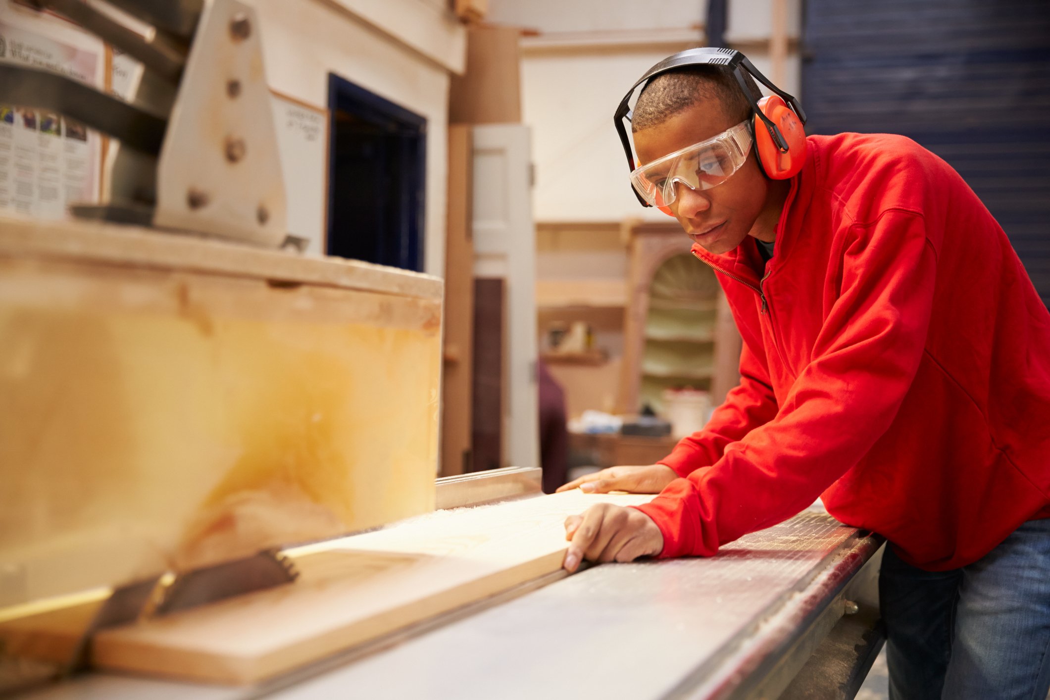 A person wearing safety goggles cuts wood with a table saw.