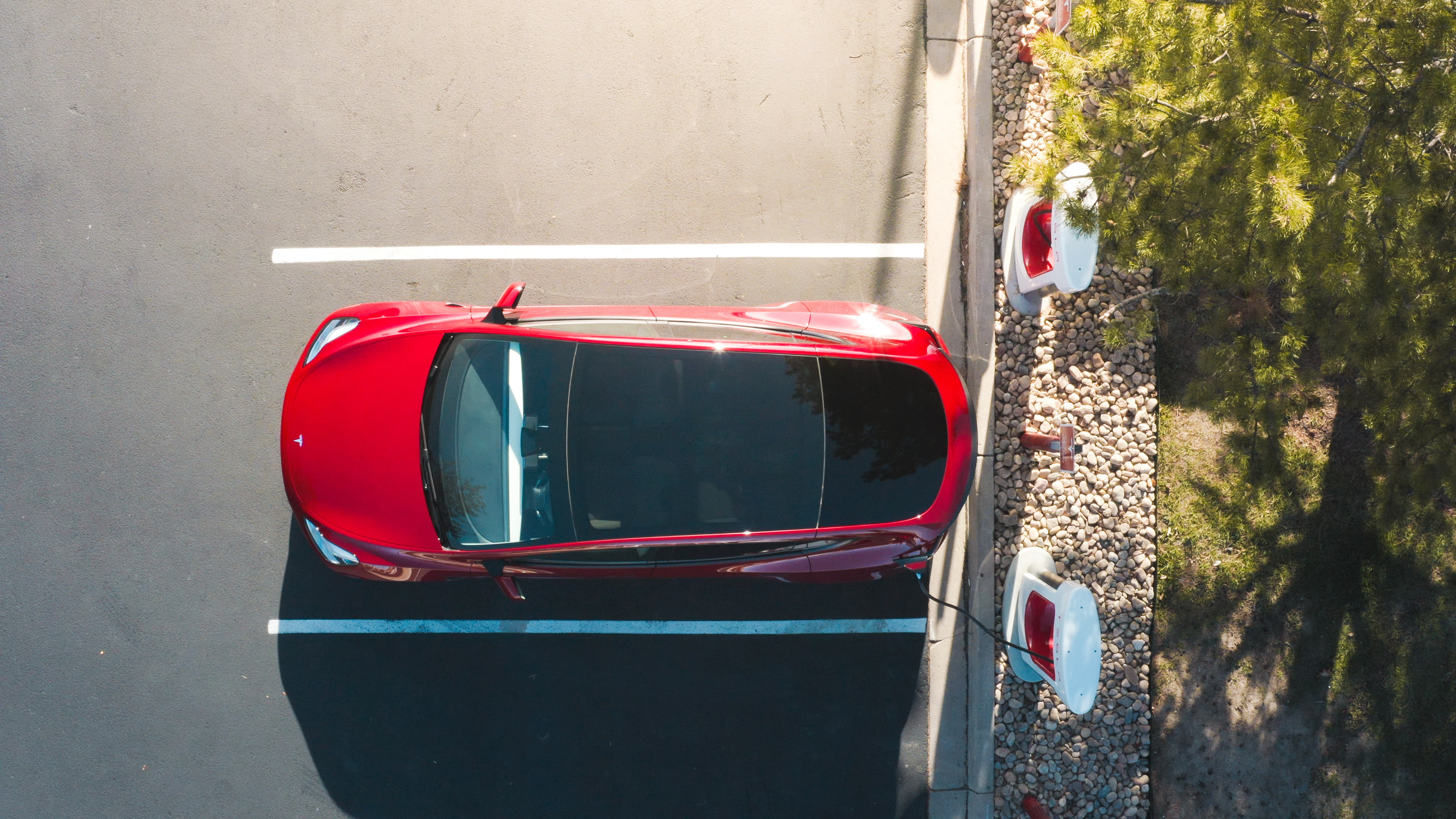 Overhead view of Tesla EV parked at supercharger. 