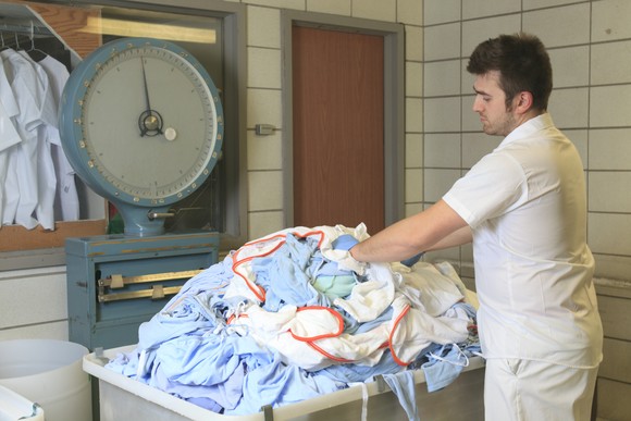 A worker loading hospital linens and laundry into a bin.