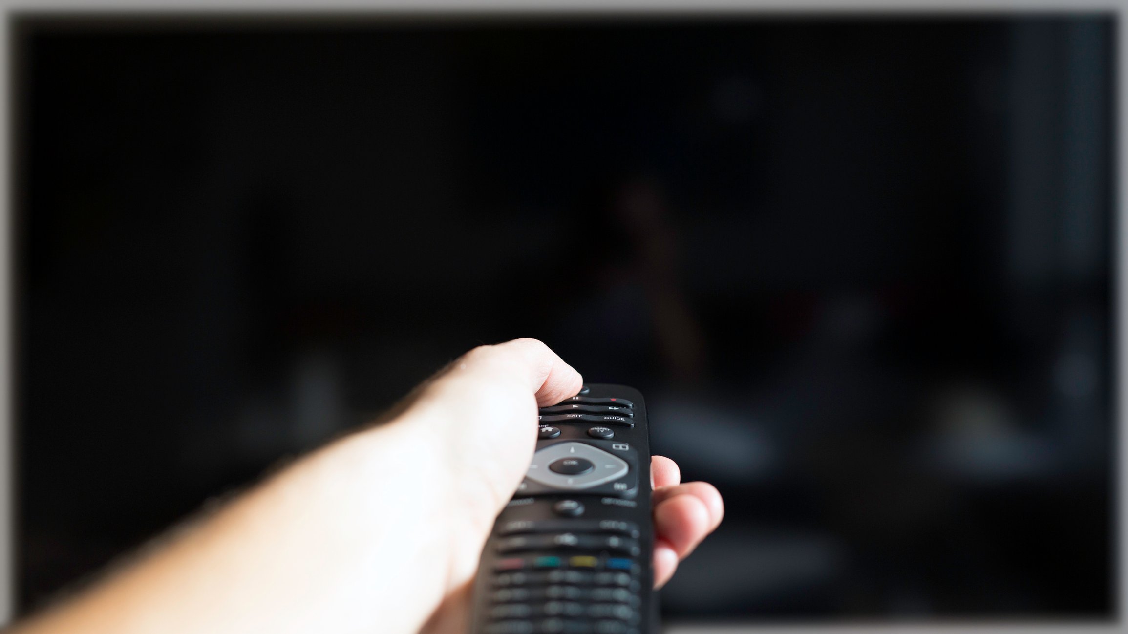 A hand holding a remote control, shutting off a TV. 