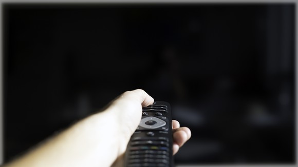 A hand holding a remote control, shutting off a TV. 