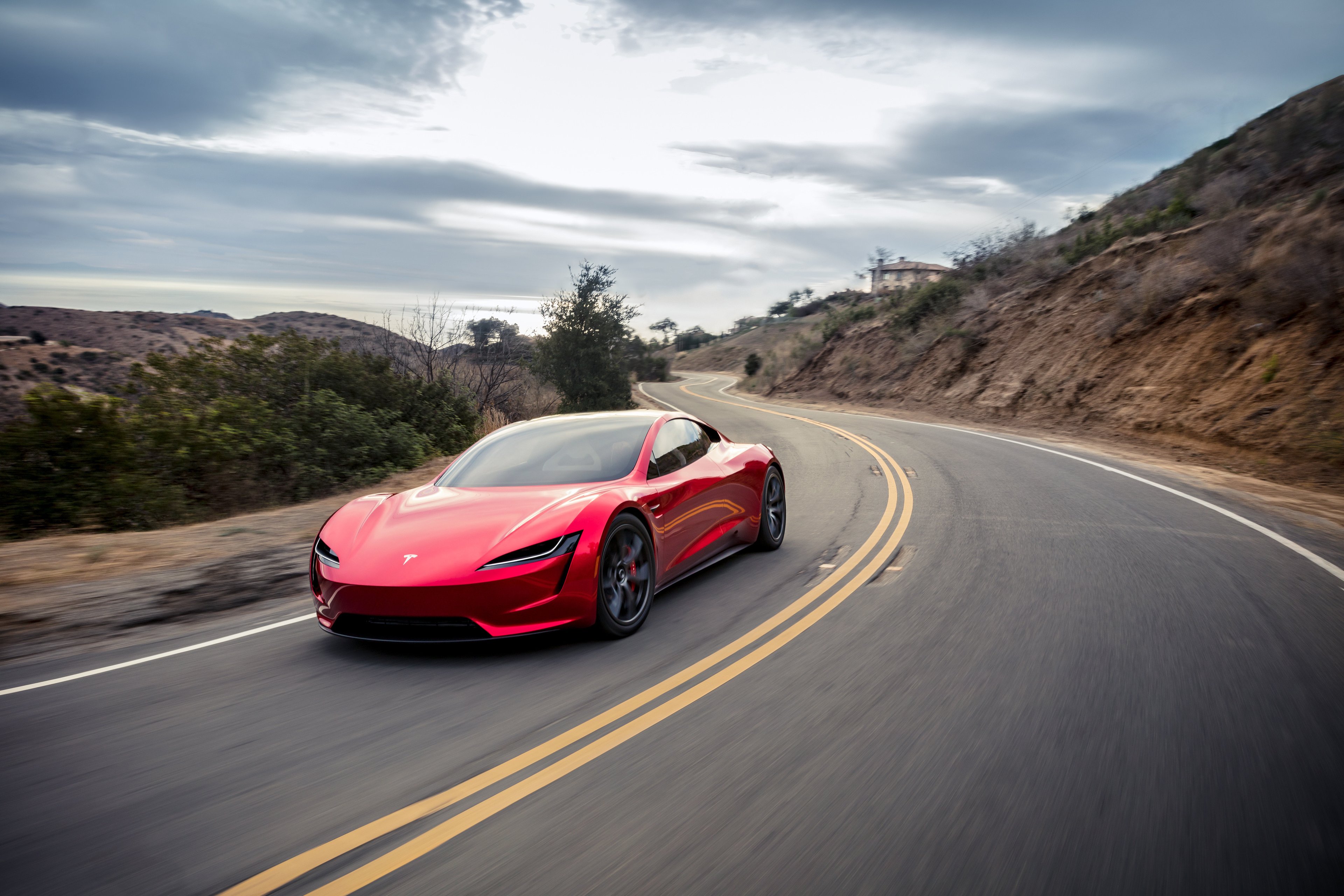 red Tesla Roadster on coastal highway.
