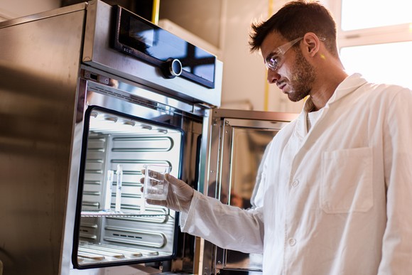 A scientist removes a clean beaker from a sterilization machine.