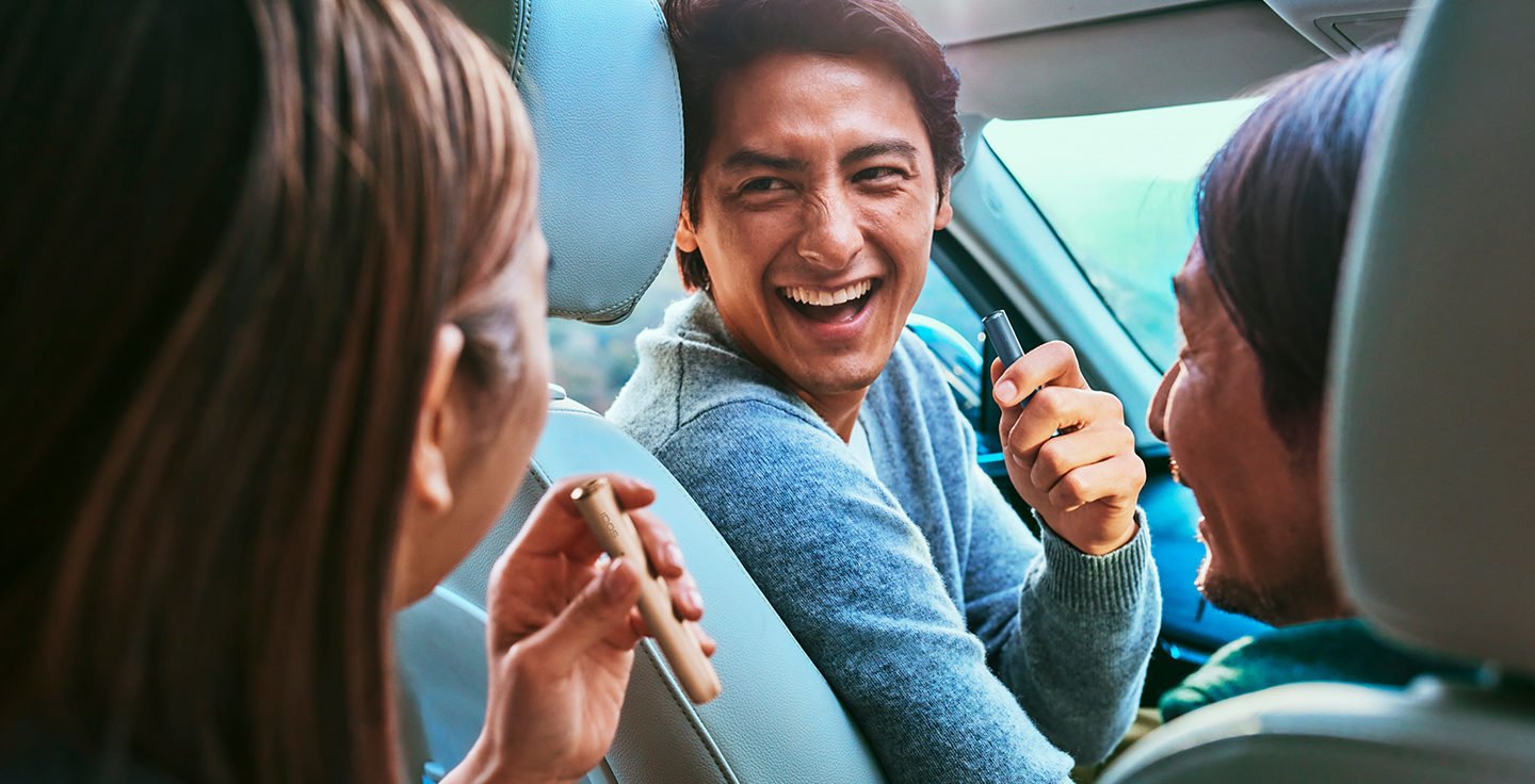 Smiling friends with IQOS heated tobacco devices.