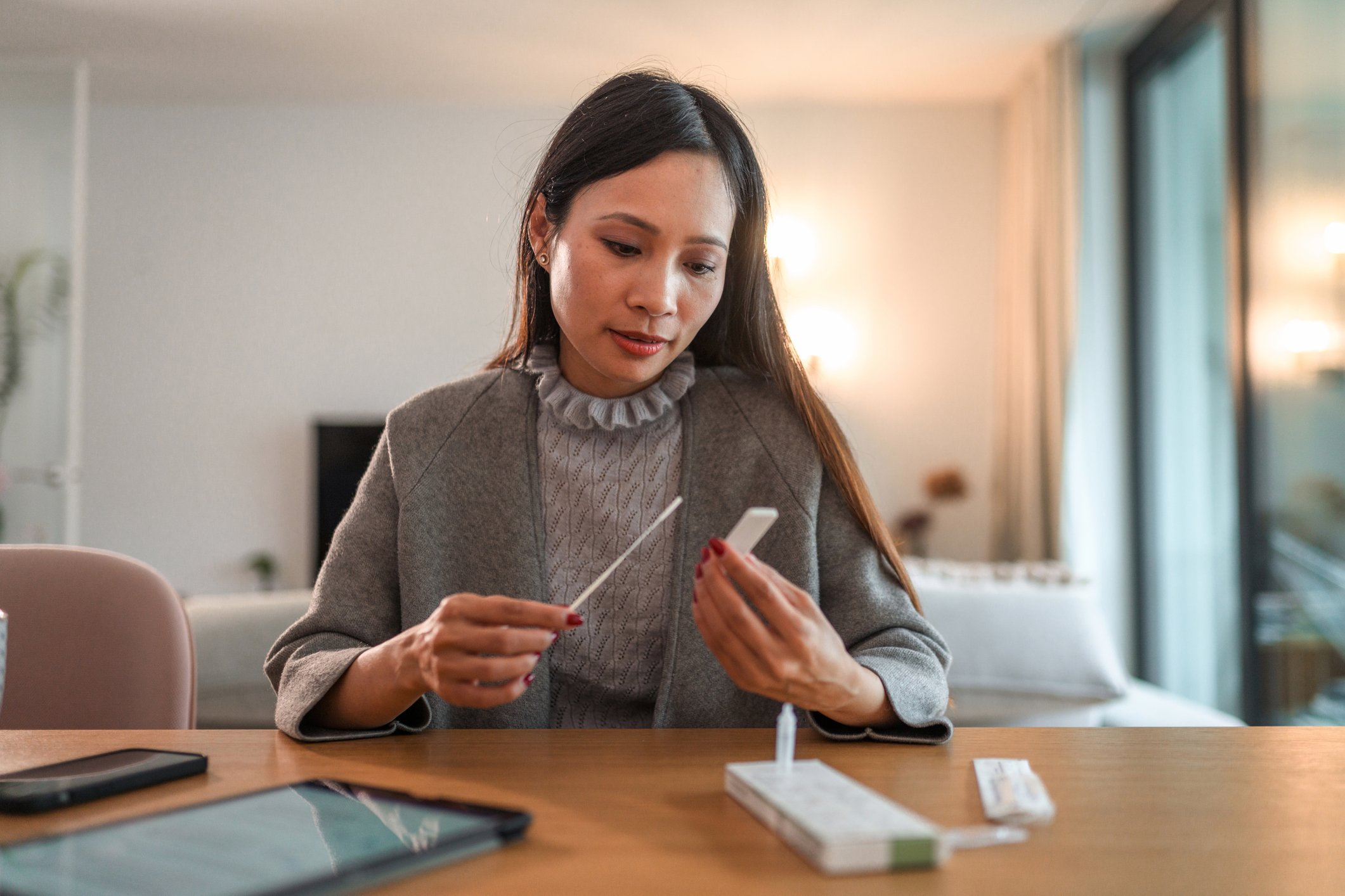 An individual sits at a table at home and checks results of an at-home coronavirus test.