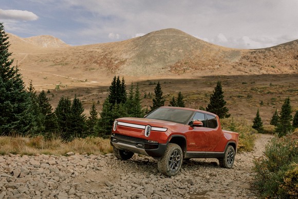 A Rivian RT pickup truck on a rocky road with  hills in the background.