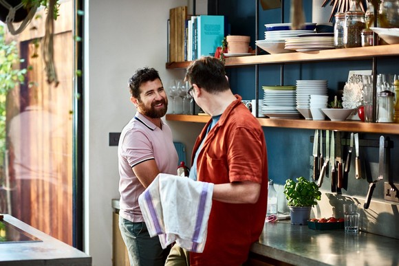 Two people smiling while drying dishes in the kitchen.
