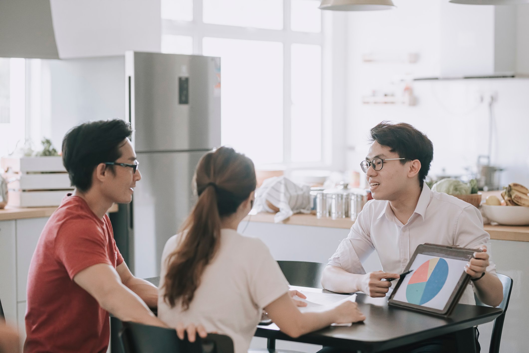 Three people sit at a table. One person is pointing to a pie chart on a tablet.