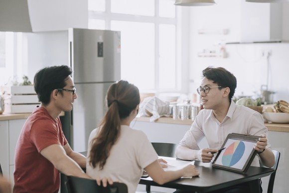 Three people sit at a table. One person is pointing to a pie chart on a tablet.