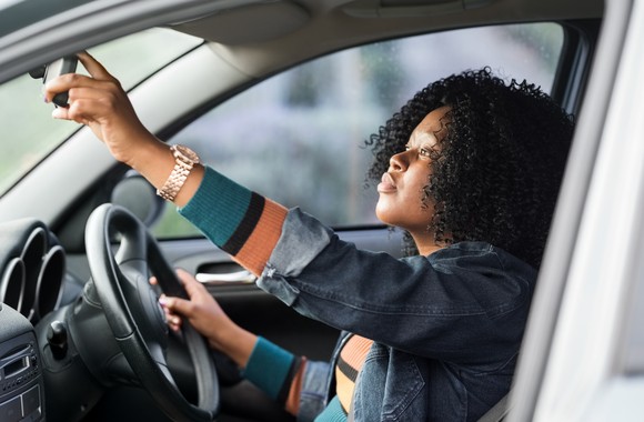 A person adjusting their rearview mirror from the driver's seat.