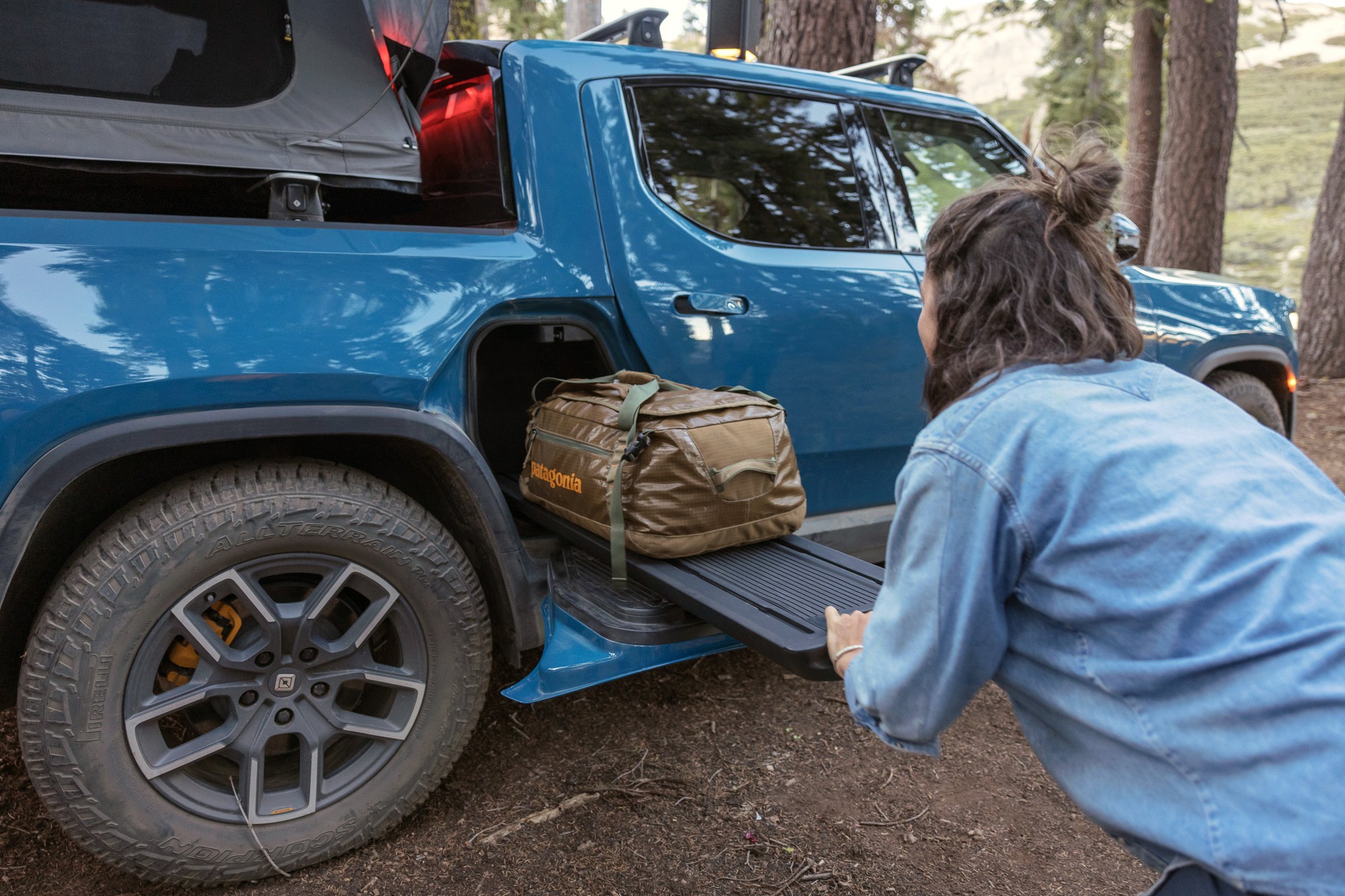 A person stowing luggage on a Rivian truck.
