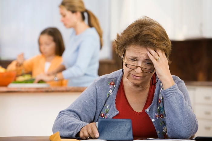 Worried senior with hand on head holding checkbook.