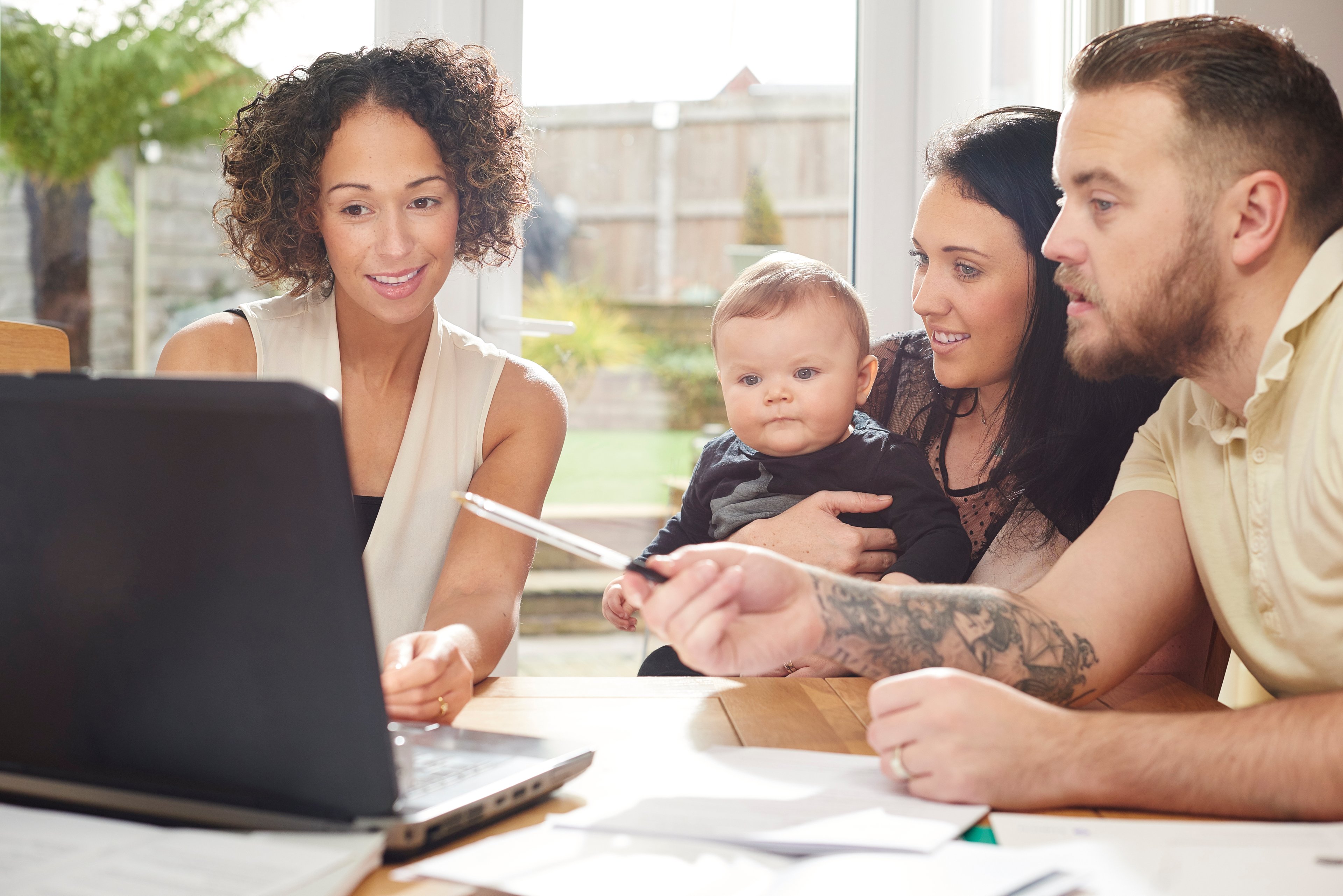 Three people and a baby gathered around a laptop in an office to review paperwork.