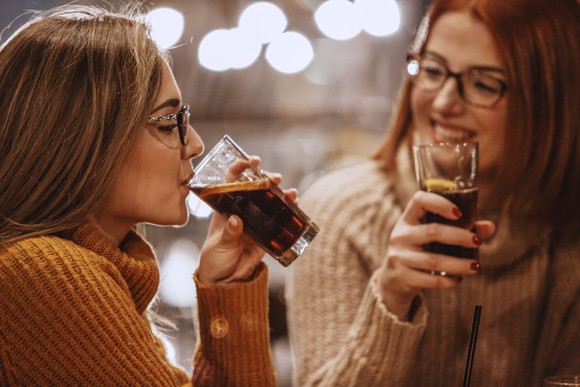Two people drinking carbonated beverages from glasses.