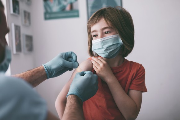 Young child in a mask receives a vaccine. 
