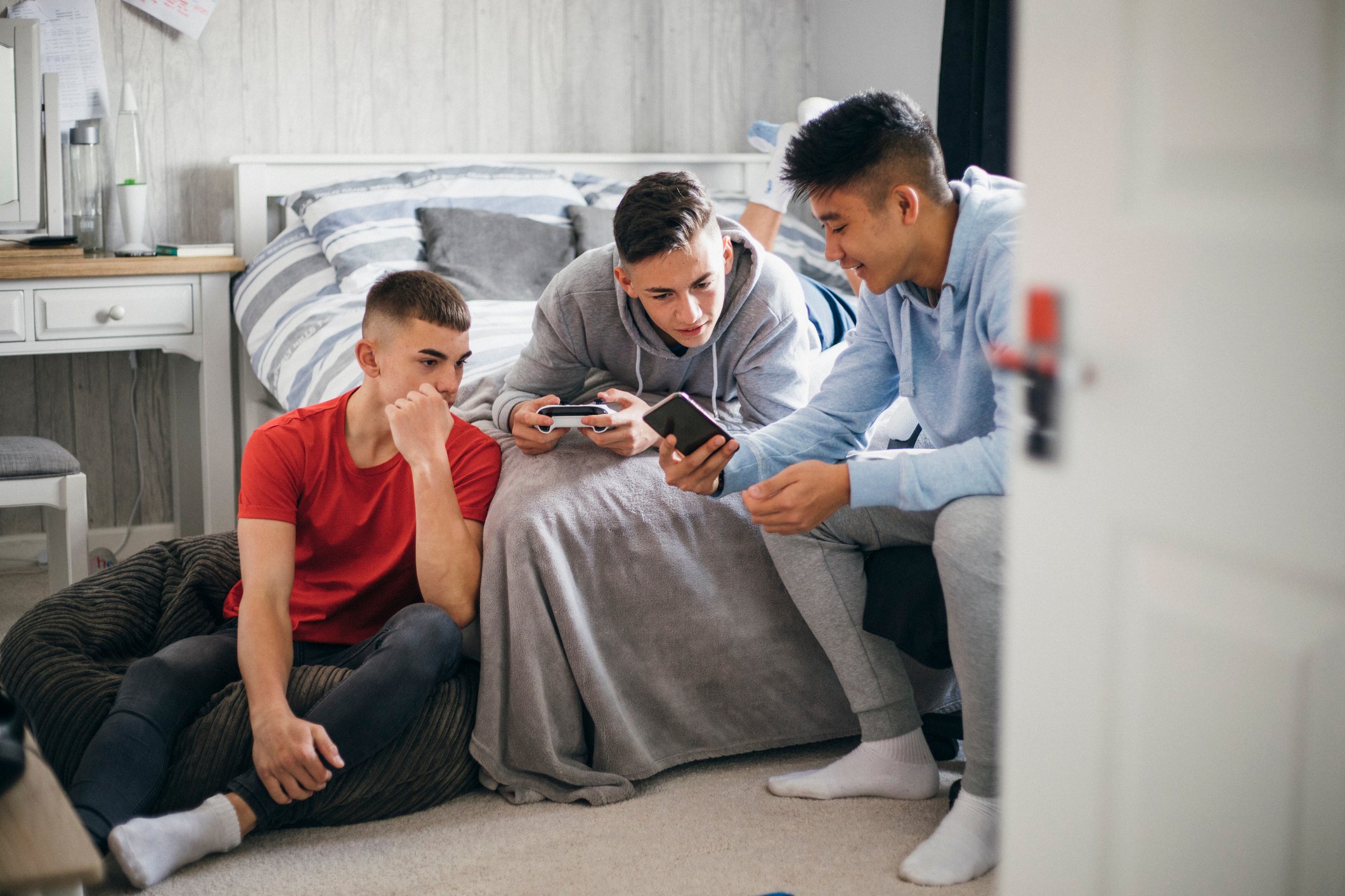 Three young people hanging out in a bedroom looking at their smart phones.