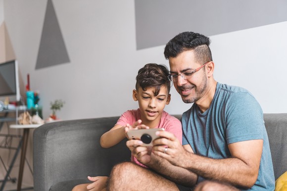 Adult and child looking at a smartphone, while sitting on a couch.
