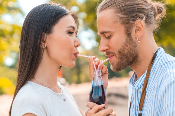 Two people drinking soda from the same soda bottle.