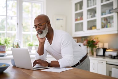 investor stands in kitchen considering laptop