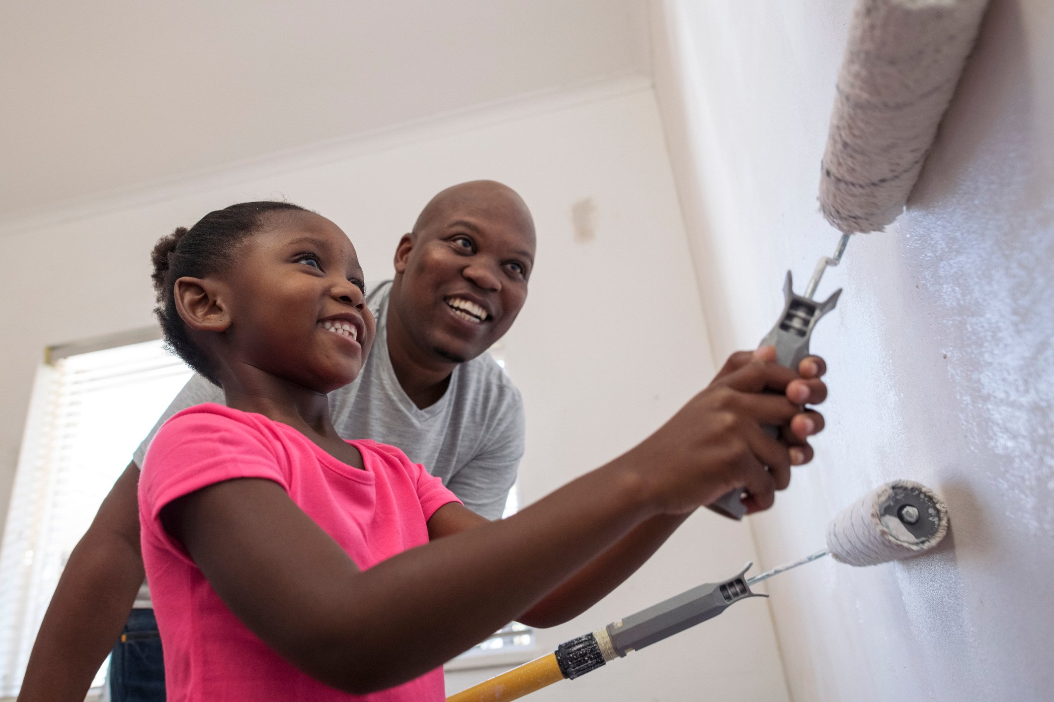 Adult and child painting a wall in a room.