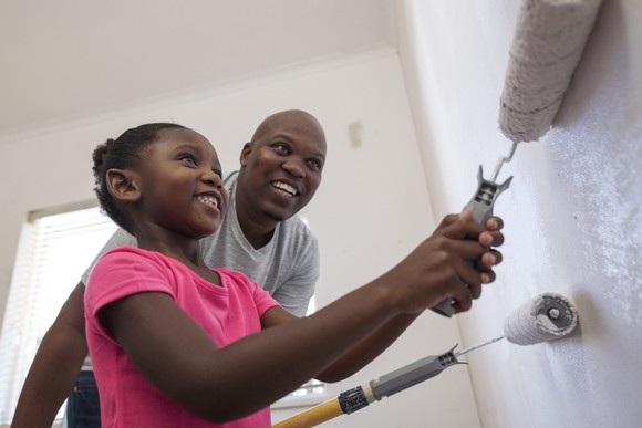 Adult and child painting a wall in a room.
