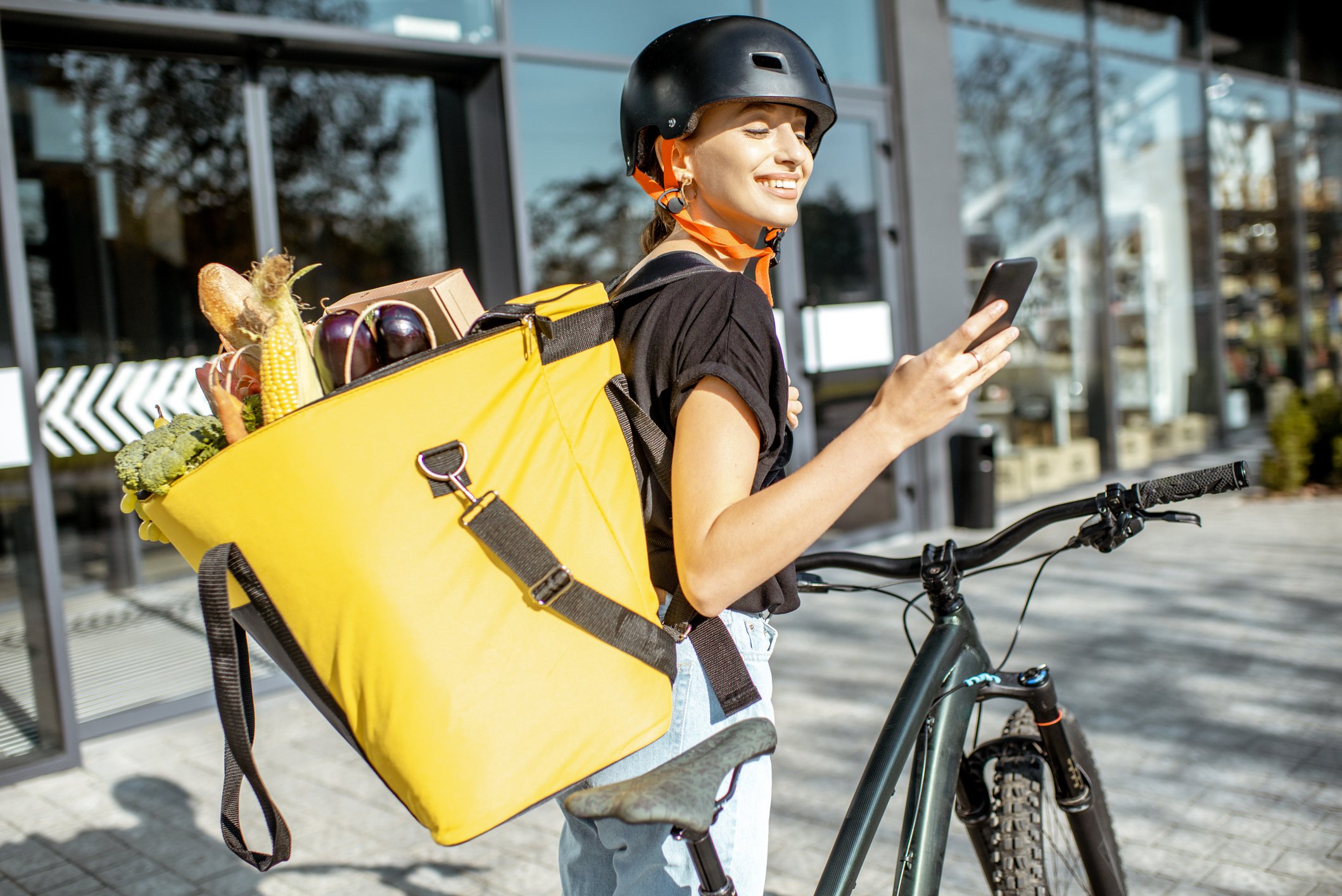 Delivery person checks smartphone while delivering groceries on a bicycle.