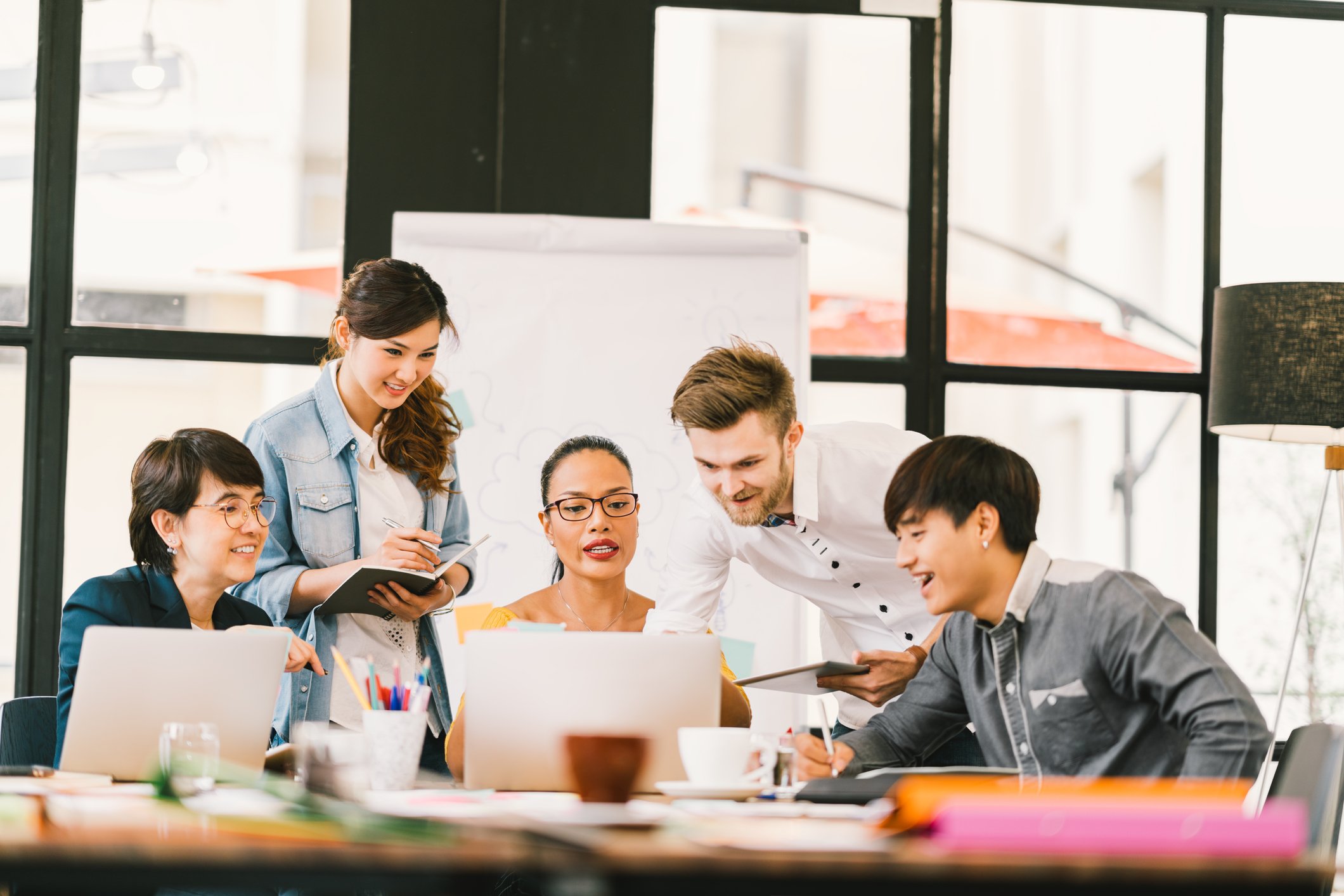Workers gather around a laptop in a meeting room.