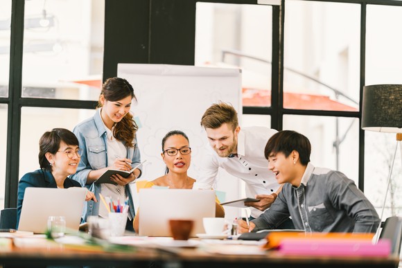 Workers gather around a laptop in a meeting room.