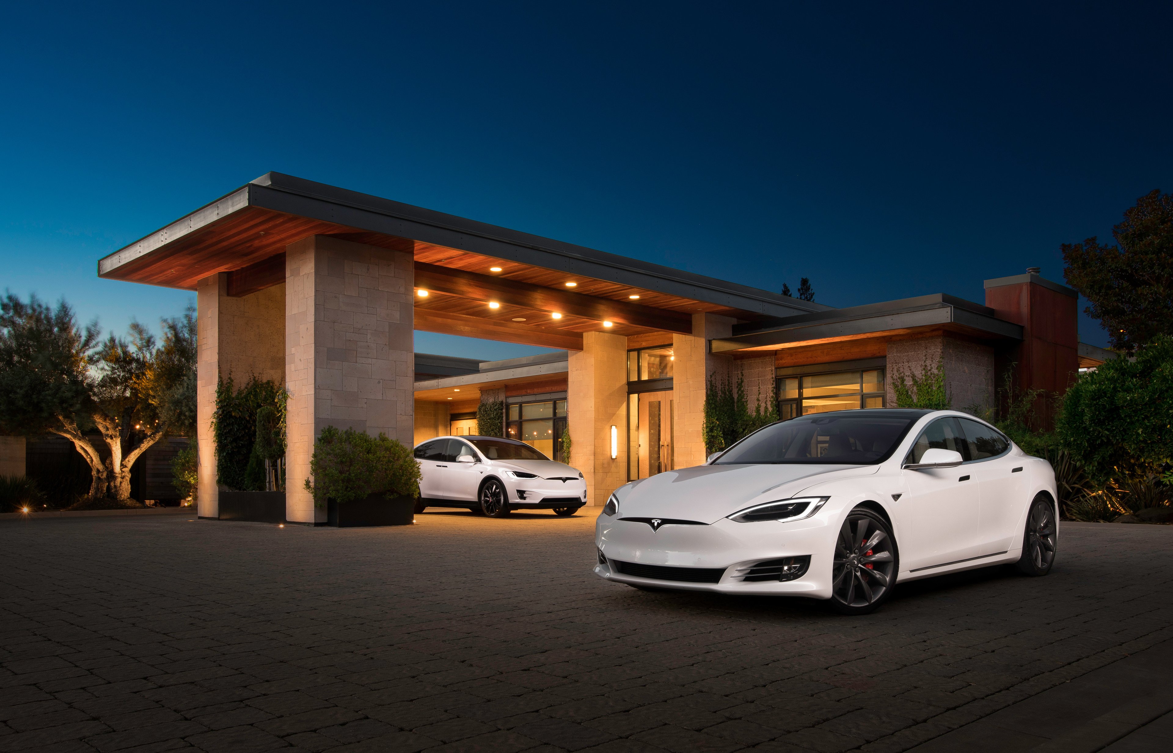 Two white Teslas parked in front of a building at twilight.